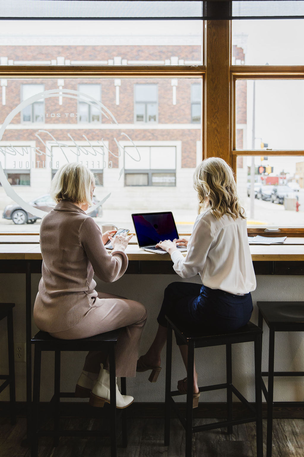 Two team members collaborating on marketing work, one reviewing content on a phone while the other works on a computer.