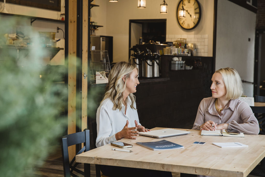 Two marketing professionals meeting in a coffee shop discussing strategy.