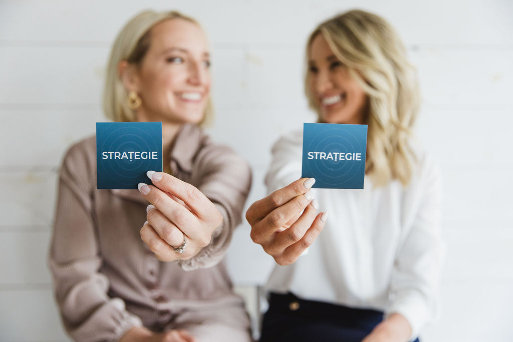 Two women smiling at each other while holding Strategie business cards.
