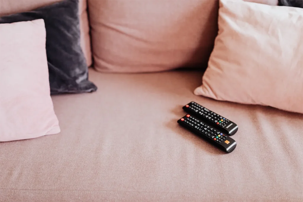 Two television remotes sitting on a sofa.