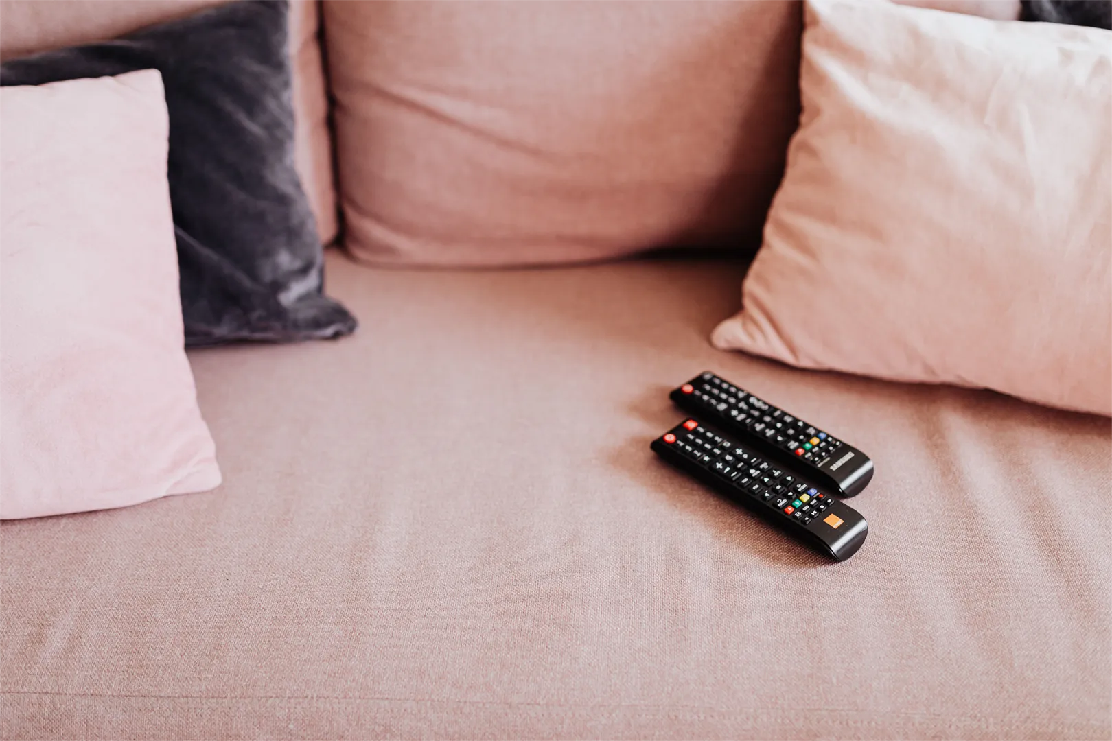 Two television remotes sitting on a sofa.